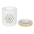 White wax burner with decorative mandala pattern and wooden base with lit candle on a white background